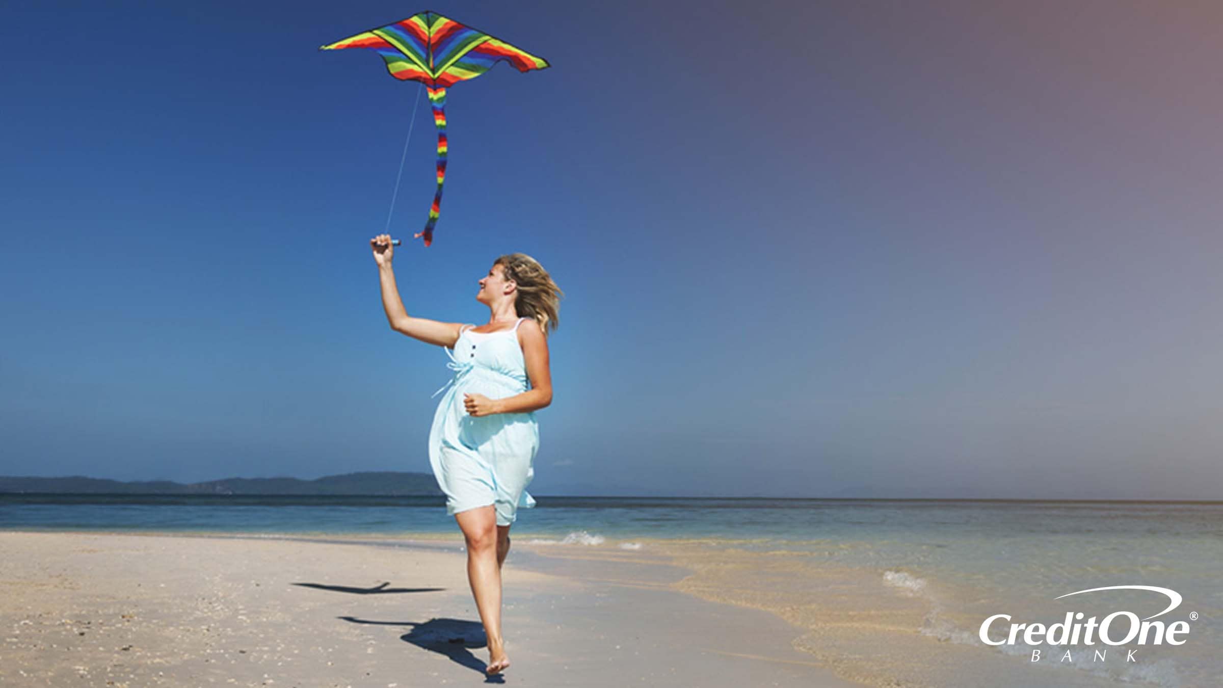 Woman running on a shoreline with a kite flying overhead